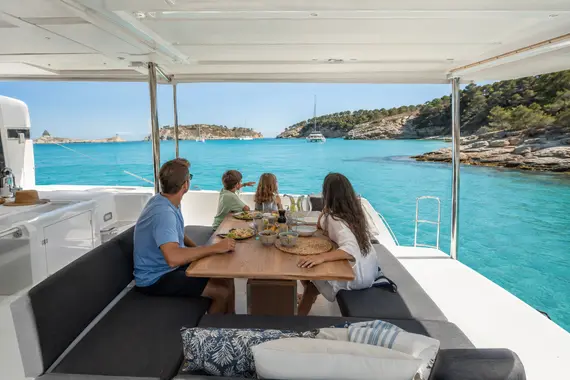 Family enjoying lunch in the shaded cockpit of a catamaran in a Mediterranean bay