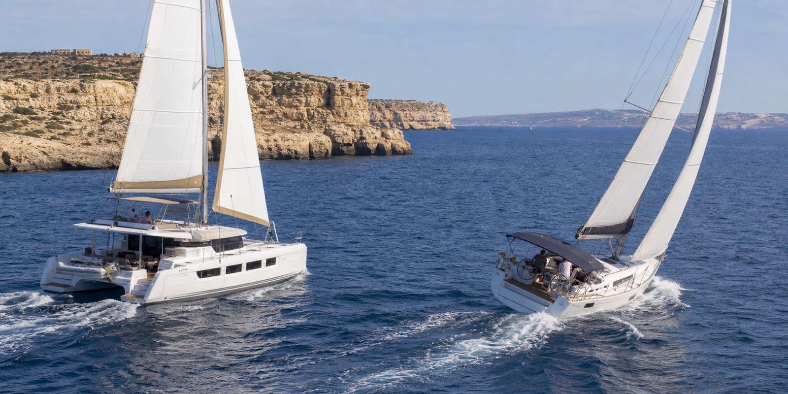 Catamaran and monohull sailing separately near Malta’s limestone coast